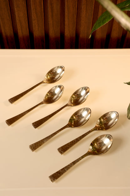 Set of silver spoons on a beige surface with a wooden background