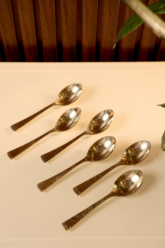 Set of silver spoons on a beige surface with a wooden background
